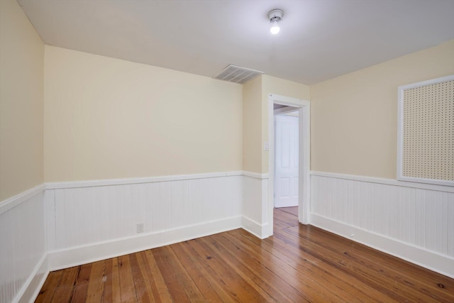 unfurnished room featuring wood-type flooring, visible vents, and a wainscoted wall