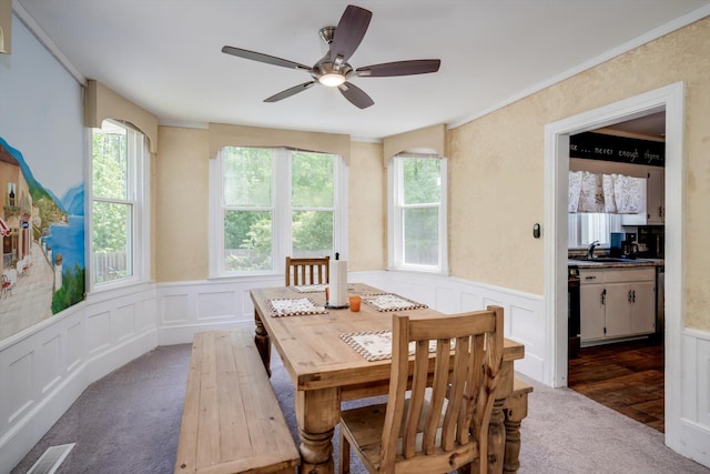 carpeted dining area featuring visible vents, ceiling fan, a wainscoted wall, and a healthy amount of sunlight