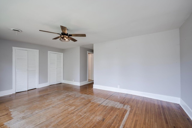 unfurnished bedroom featuring ceiling fan, hardwood / wood-style floors, two closets, baseboards, and visible vents