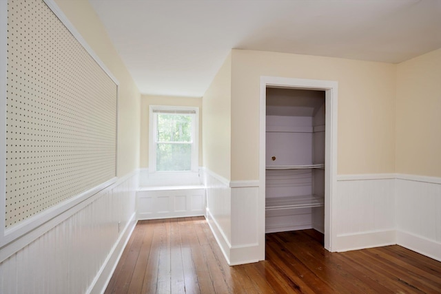 hallway featuring wainscoting, a decorative wall, and hardwood / wood-style flooring