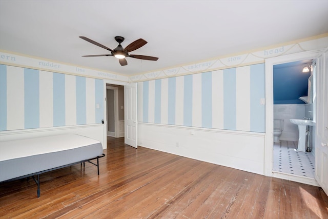 bedroom featuring a sink, wood-type flooring, wainscoting, and wallpapered walls
