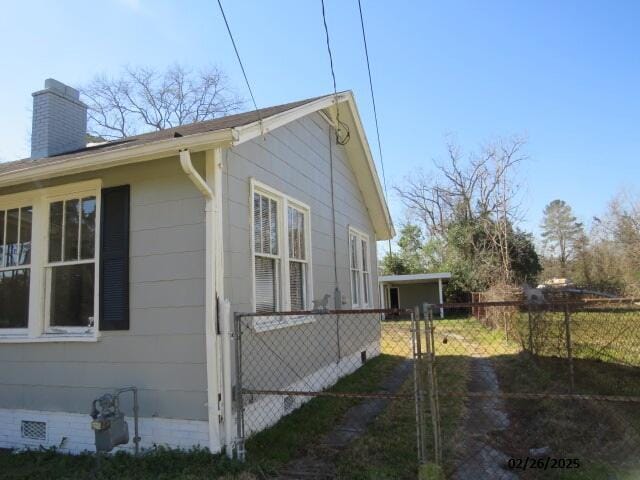 view of side of property featuring crawl space, a chimney, fence, and a gate