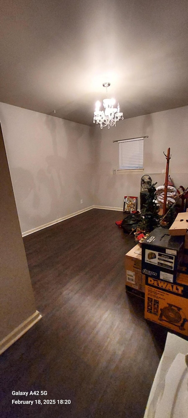 unfurnished dining area with an inviting chandelier, baseboards, and dark wood-style floors