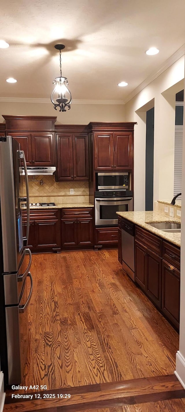 kitchen with light stone counters, wood finished floors, stainless steel appliances, under cabinet range hood, and a sink