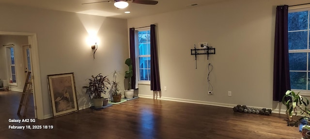 interior space with baseboards, visible vents, a ceiling fan, and dark wood-type flooring