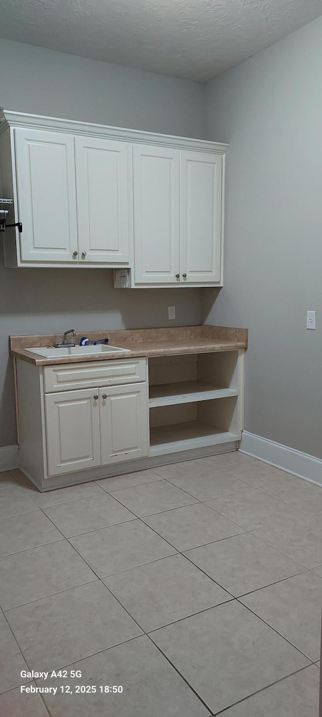 kitchen with light tile patterned floors, baseboards, white cabinetry, and a textured ceiling