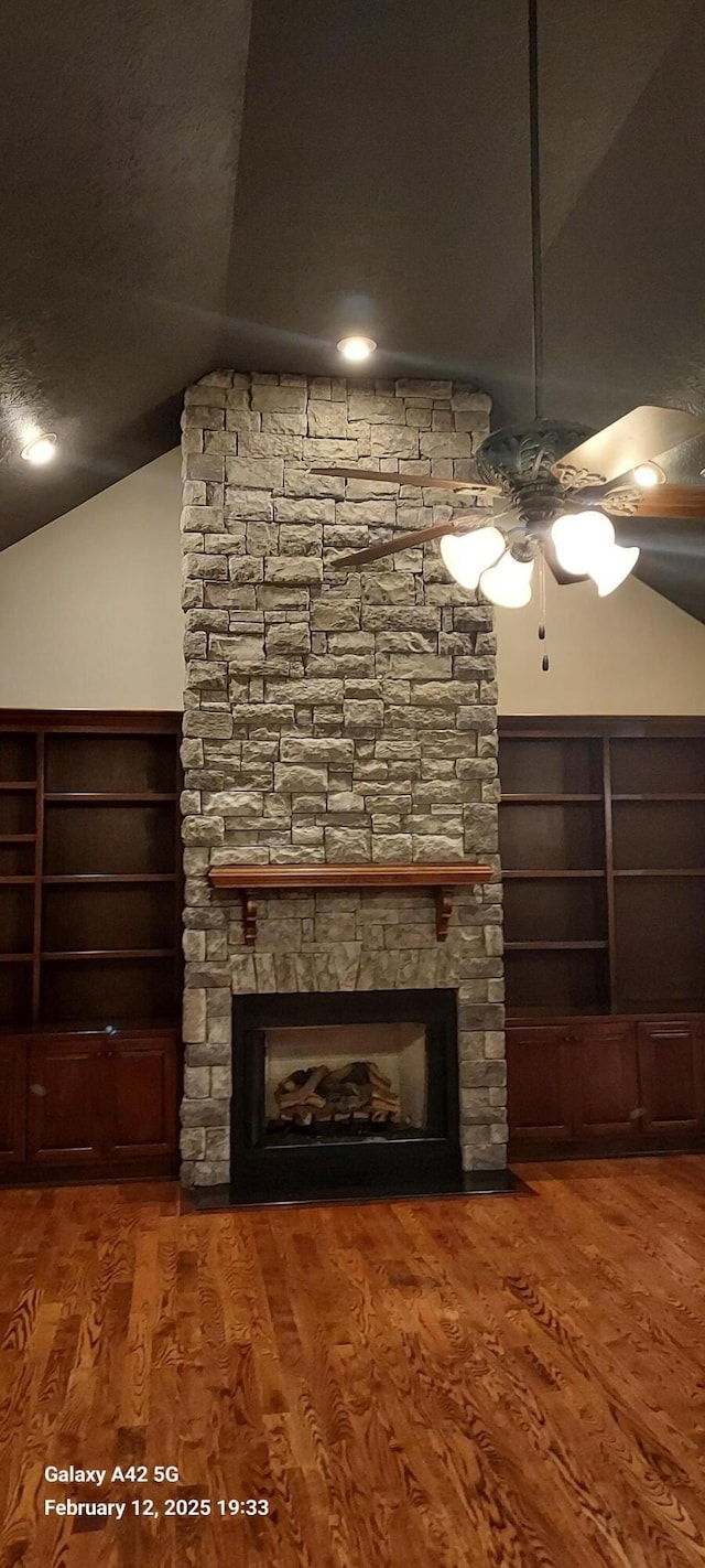 unfurnished living room featuring lofted ceiling, ceiling fan, a stone fireplace, and wood finished floors