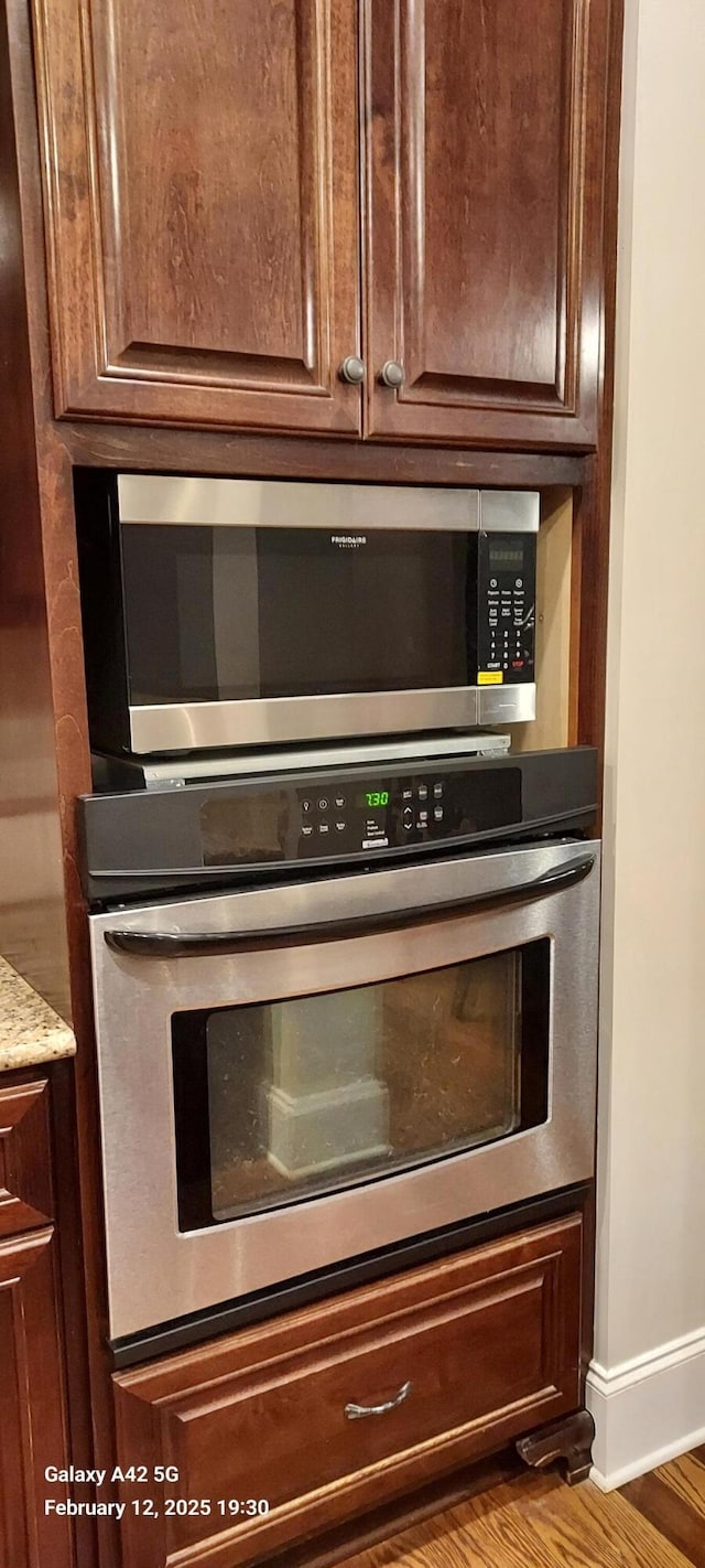 interior details with appliances with stainless steel finishes, wood finished floors, light stone counters, and baseboards