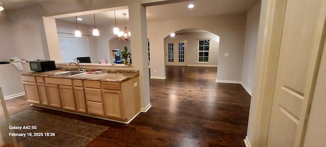 kitchen featuring arched walkways, hanging light fixtures, light brown cabinets, a sink, and baseboards