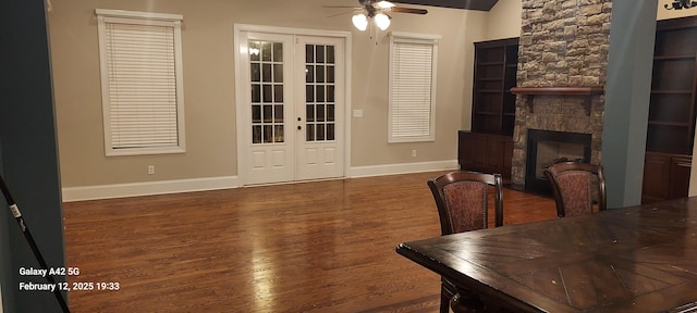 interior space with french doors, dark wood-style flooring, a fireplace, ceiling fan, and baseboards