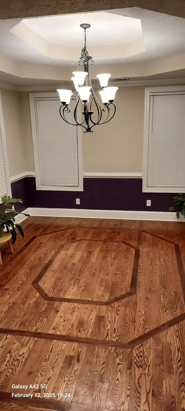 unfurnished dining area with baseboards, a raised ceiling, wood finished floors, and an inviting chandelier