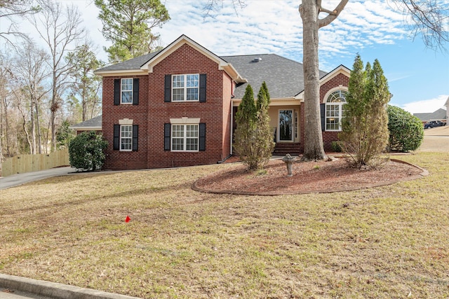 view of front of house featuring a front lawn, fence, brick siding, and roof with shingles