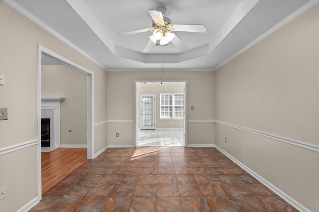 unfurnished room with baseboards, a raised ceiling, ceiling fan, and a fireplace