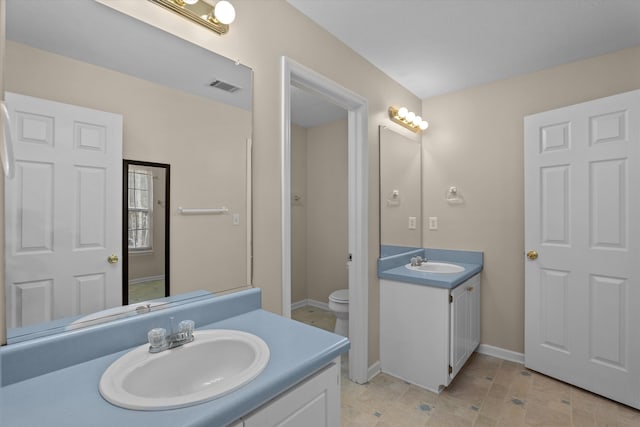 bathroom with visible vents, toilet, two vanities, and a sink