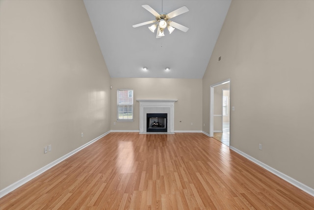 unfurnished living room with a ceiling fan, baseboards, high vaulted ceiling, a fireplace, and light wood-style floors