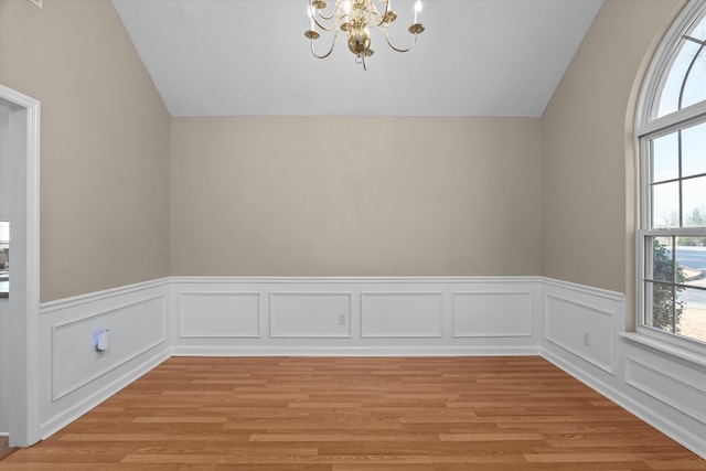 unfurnished dining area with vaulted ceiling, a notable chandelier, and light wood-type flooring