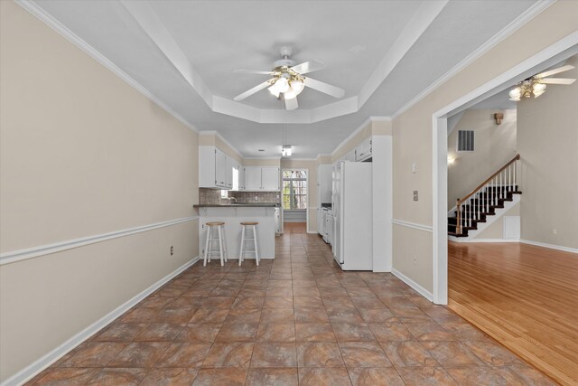 kitchen featuring visible vents, a peninsula, freestanding refrigerator, ceiling fan, and a raised ceiling