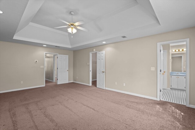 empty room featuring a raised ceiling, carpet flooring, baseboards, and ceiling fan