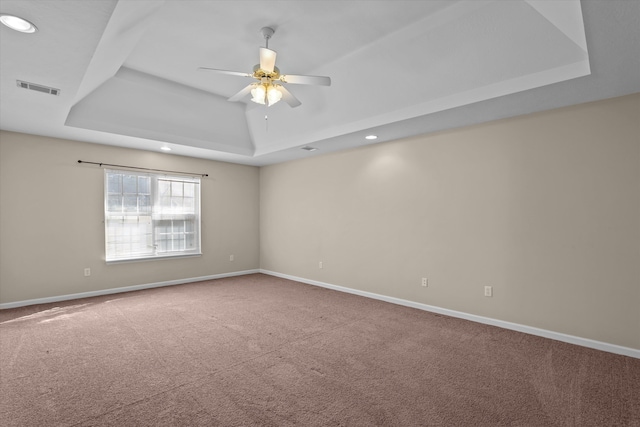 carpeted spare room with visible vents, ceiling fan, baseboards, and a tray ceiling