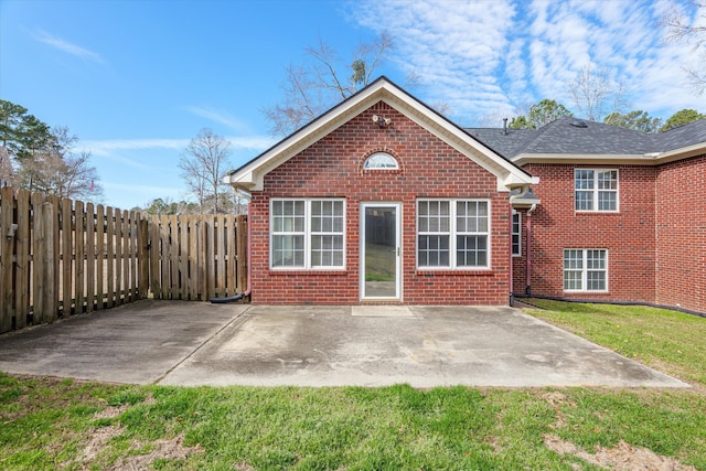 back of property featuring fence, brick siding, a lawn, and a patio area