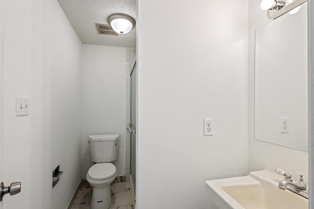 bathroom featuring a textured ceiling, toilet, a sink, visible vents, and a shower with door