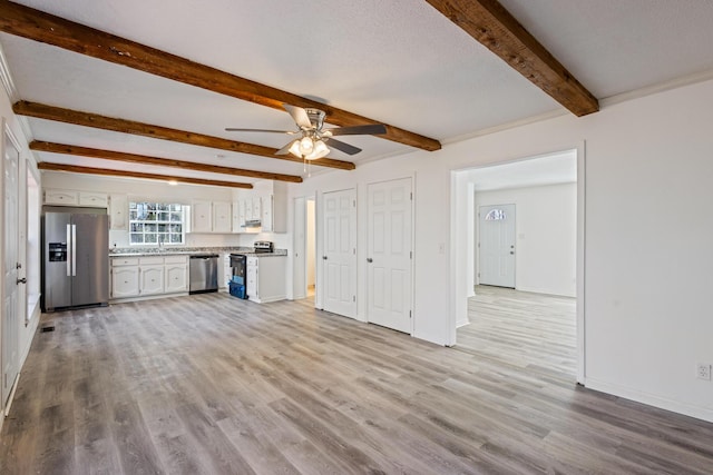 unfurnished living room with baseboards, a ceiling fan, beamed ceiling, light wood-style floors, and a sink