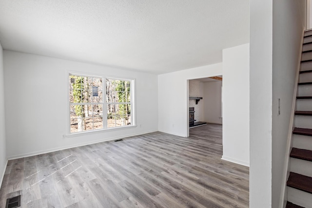 unfurnished room featuring stairway, a fireplace, visible vents, and light wood-style floors