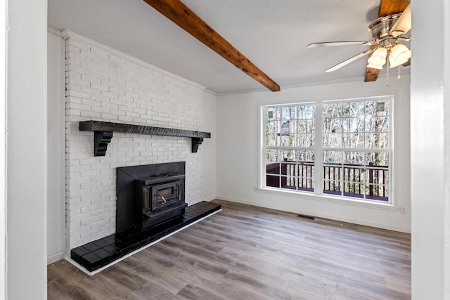 unfurnished living room with wood finished floors, visible vents, baseboards, beam ceiling, and a wood stove