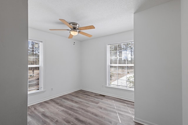 empty room with light wood finished floors, visible vents, baseboards, ceiling fan, and a textured ceiling