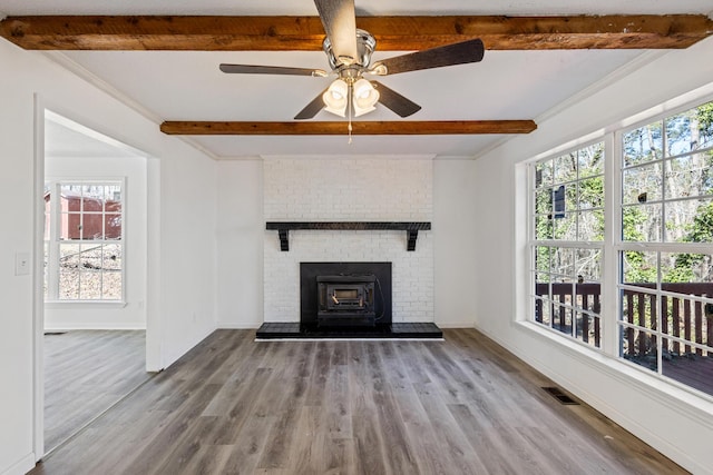 unfurnished living room with a wealth of natural light, light wood-style flooring, beamed ceiling, and visible vents