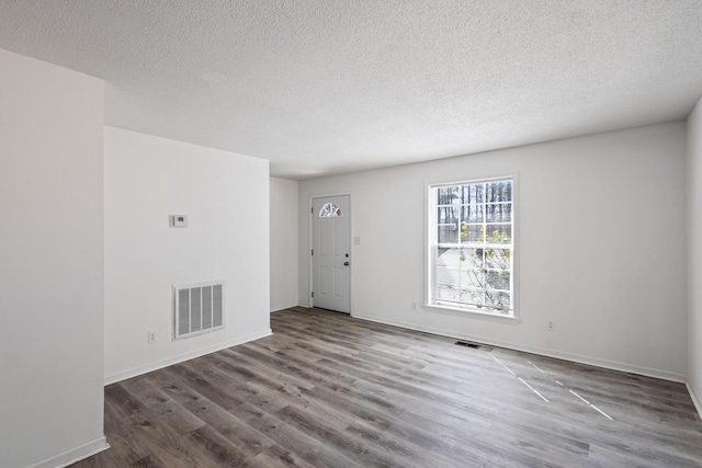 unfurnished room with visible vents, a textured ceiling, baseboards, and wood finished floors