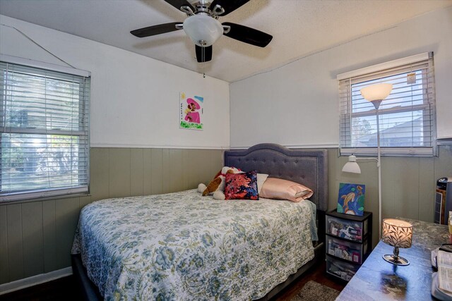 bedroom featuring ceiling fan, dark wood-type flooring, and wood walls