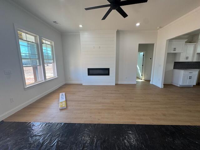 unfurnished living room featuring crown molding, a large fireplace, ceiling fan, and light hardwood / wood-style flooring