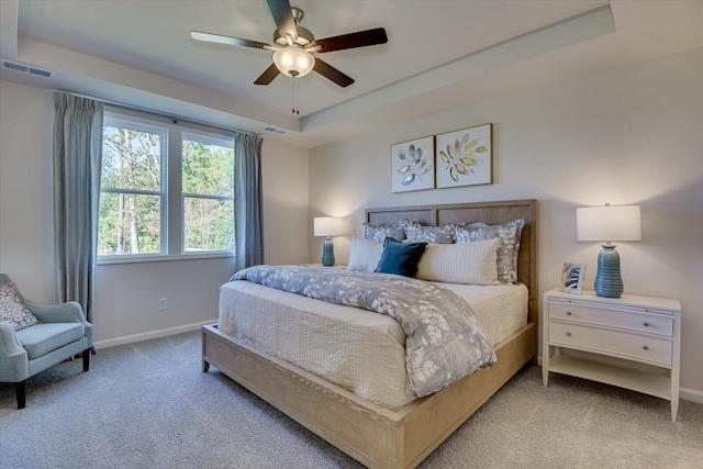 carpeted bedroom with baseboards, visible vents, a raised ceiling, and a ceiling fan