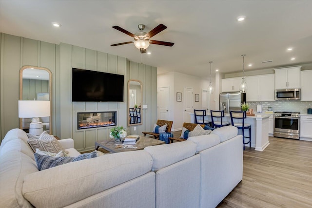 living room with ceiling fan, light wood-type flooring, a fireplace, and recessed lighting