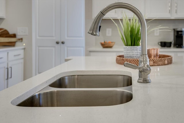 room details featuring light stone counters, a sink, and white cabinetry