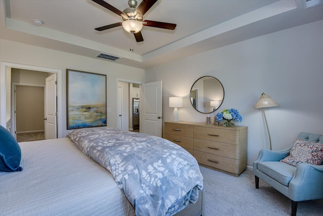 bedroom with light carpet, visible vents, a raised ceiling, and a ceiling fan