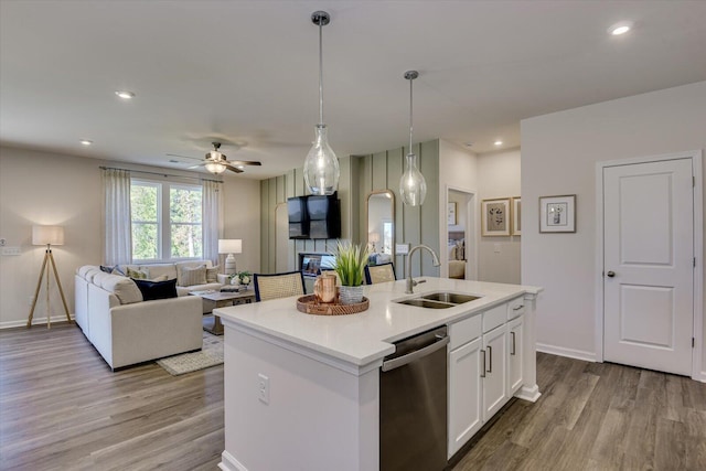 kitchen featuring open floor plan, wood finished floors, stainless steel dishwasher, white cabinetry, and a sink