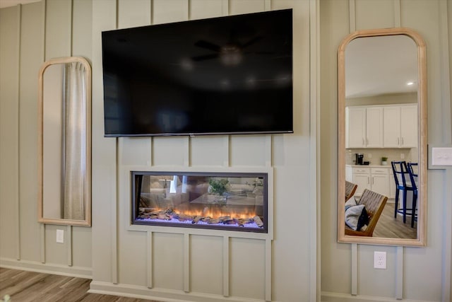 room details featuring a glass covered fireplace, a decorative wall, and wood finished floors