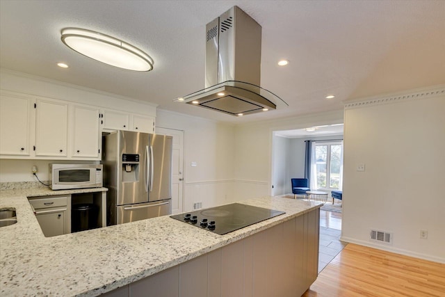 kitchen with white microwave, visible vents, stainless steel fridge with ice dispenser, black electric stovetop, and island range hood