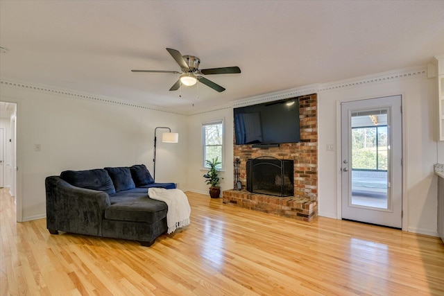 living area featuring light wood finished floors, plenty of natural light, a brick fireplace, and a ceiling fan