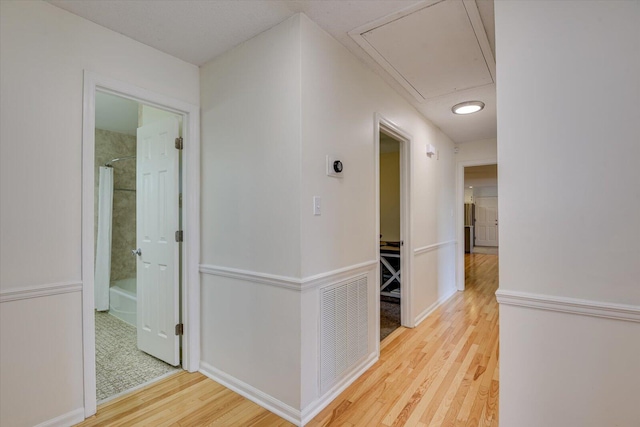 hallway featuring visible vents, attic access, baseboards, and wood finished floors