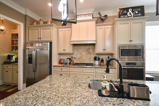 kitchen featuring appliances with stainless steel finishes, crown molding, sink, cream cabinets, and pendant lighting