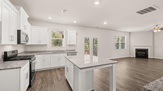 kitchen with visible vents, open floor plan, a glass covered fireplace, stainless steel appliances, and a sink