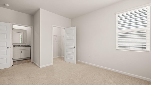 unfurnished bedroom with light carpet, a spacious closet, baseboards, and a closet