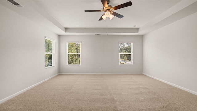 spare room featuring visible vents, a raised ceiling, light colored carpet, and baseboards