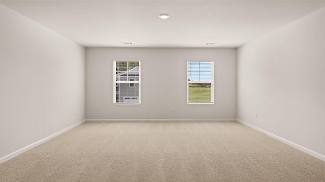 empty room with a healthy amount of sunlight, baseboards, and light carpet