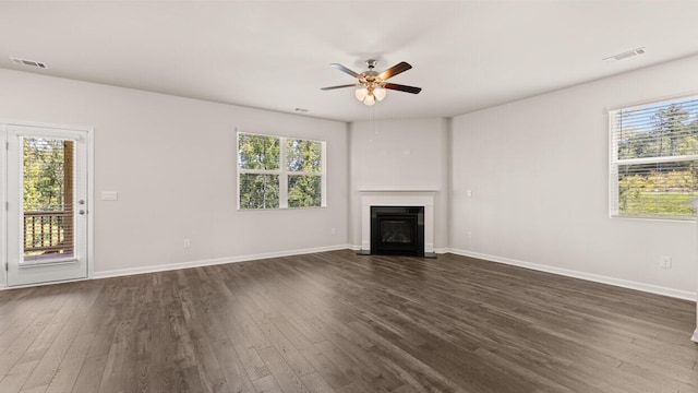 unfurnished living room with plenty of natural light, baseboards, dark wood-type flooring, and a fireplace with flush hearth