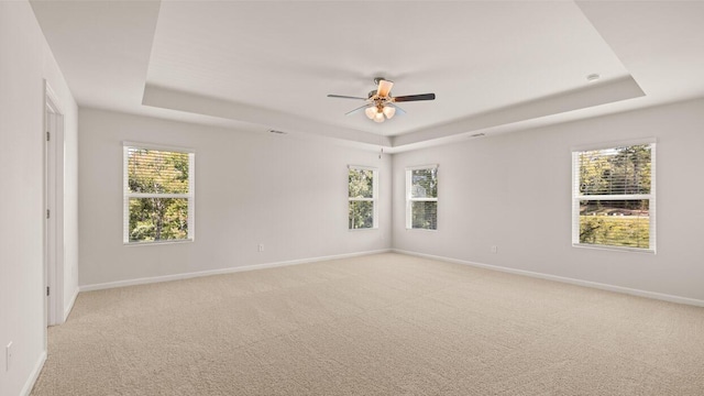 empty room with baseboards, a raised ceiling, light colored carpet, and a ceiling fan