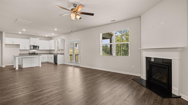 unfurnished living room with dark wood finished floors, visible vents, baseboards, and ceiling fan